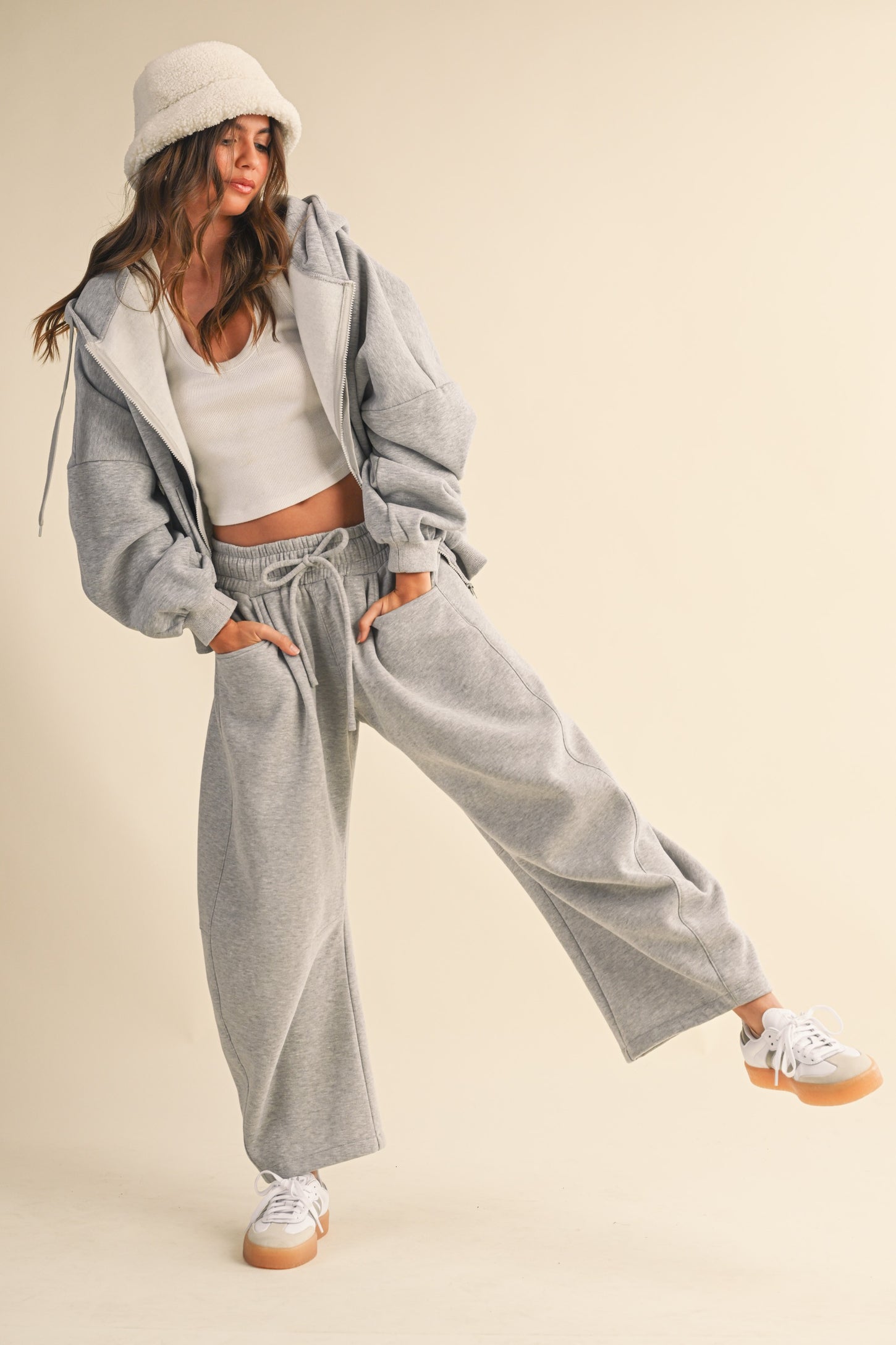 woman wearing a grey oversized hoodie and matching sweatpants with a white crop top and a beige bucket hat