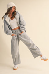woman wearing a grey oversized hoodie and matching sweatpants with a white crop top and a beige bucket hat
