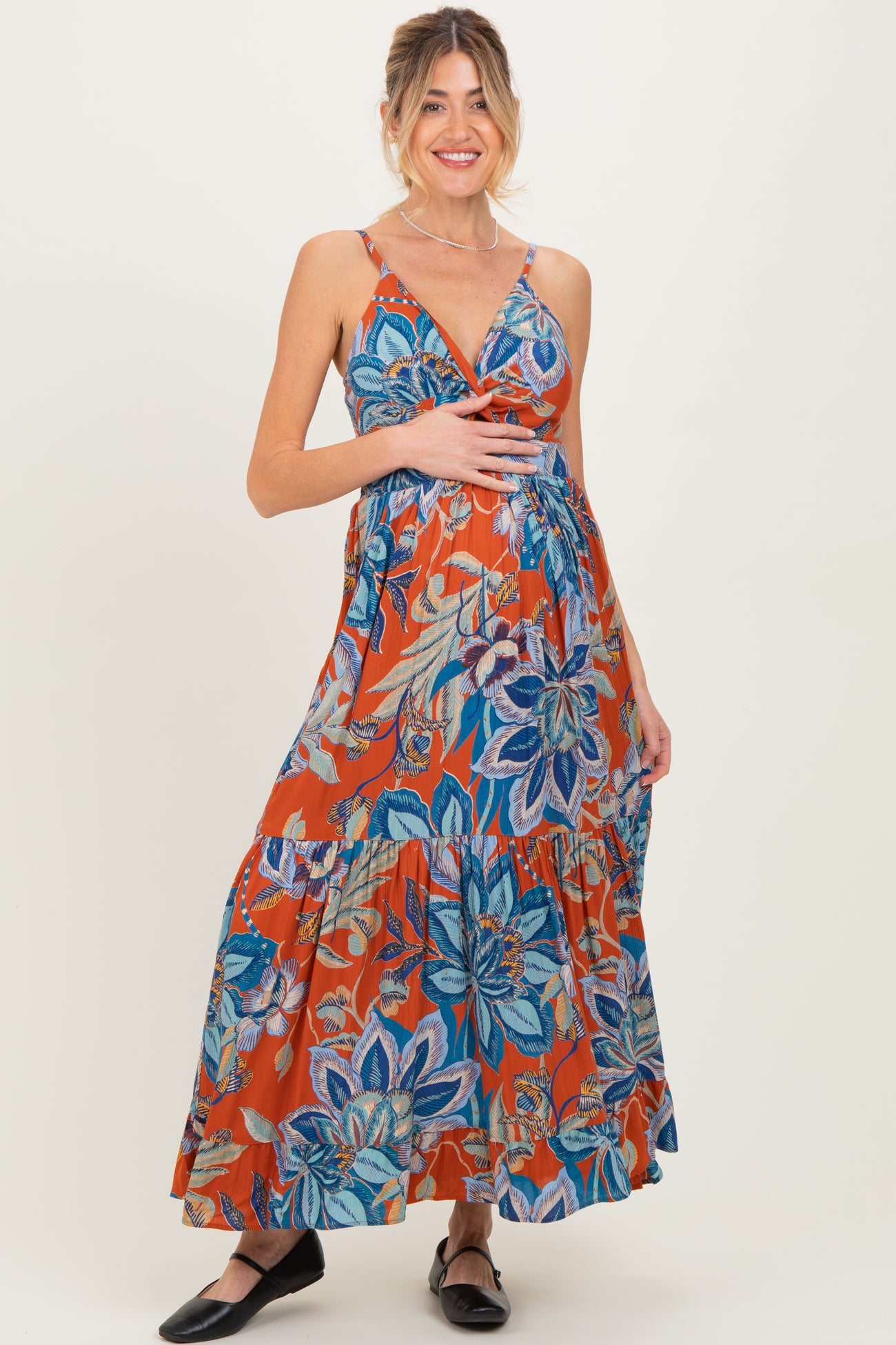 woman wearing a vibrant orange floral maternity maxi dress and holding her baby bump