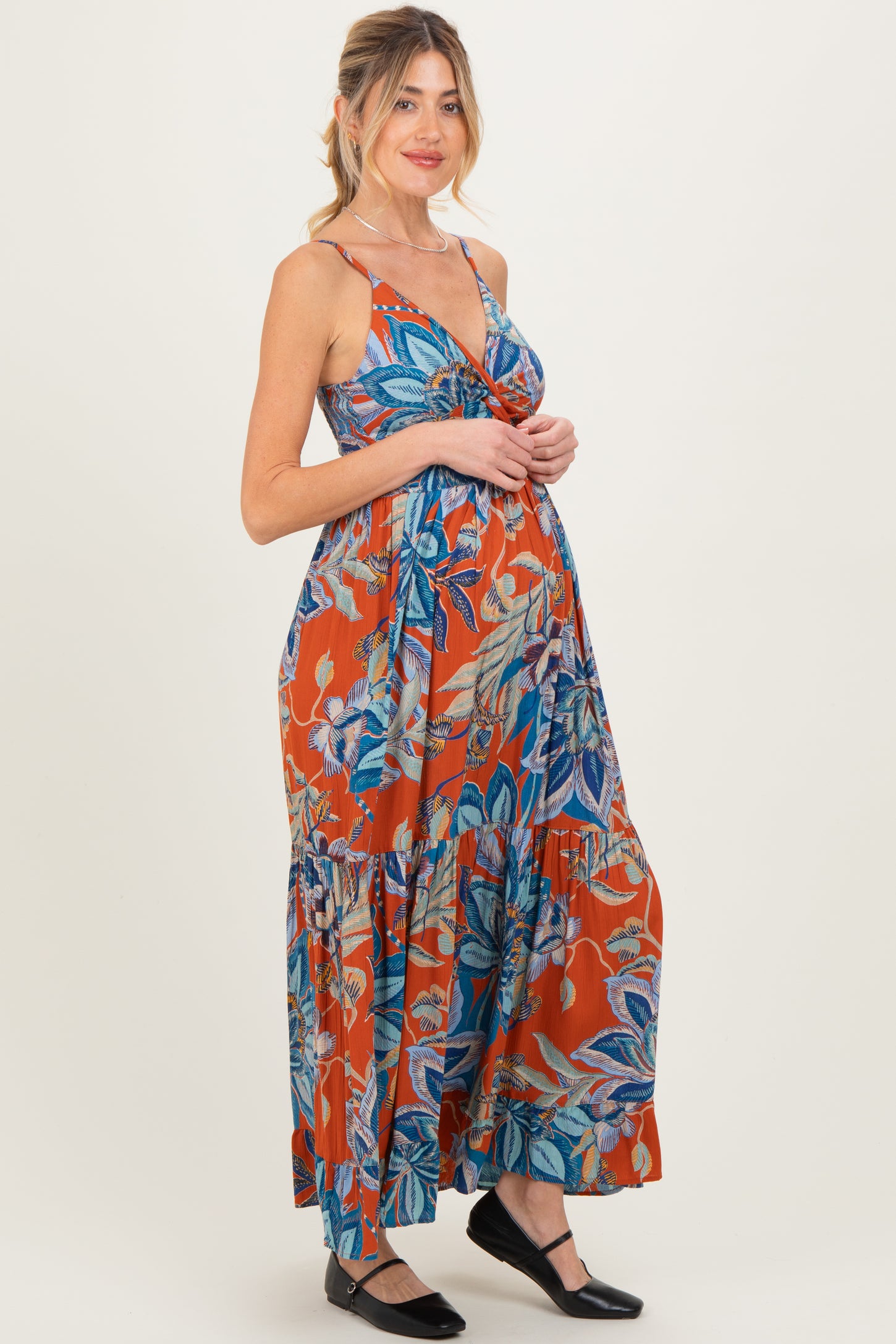 woman wearing an orange floral maternity maxi dress with a tiered skirt and spaghetti straps, showing her baby bump
