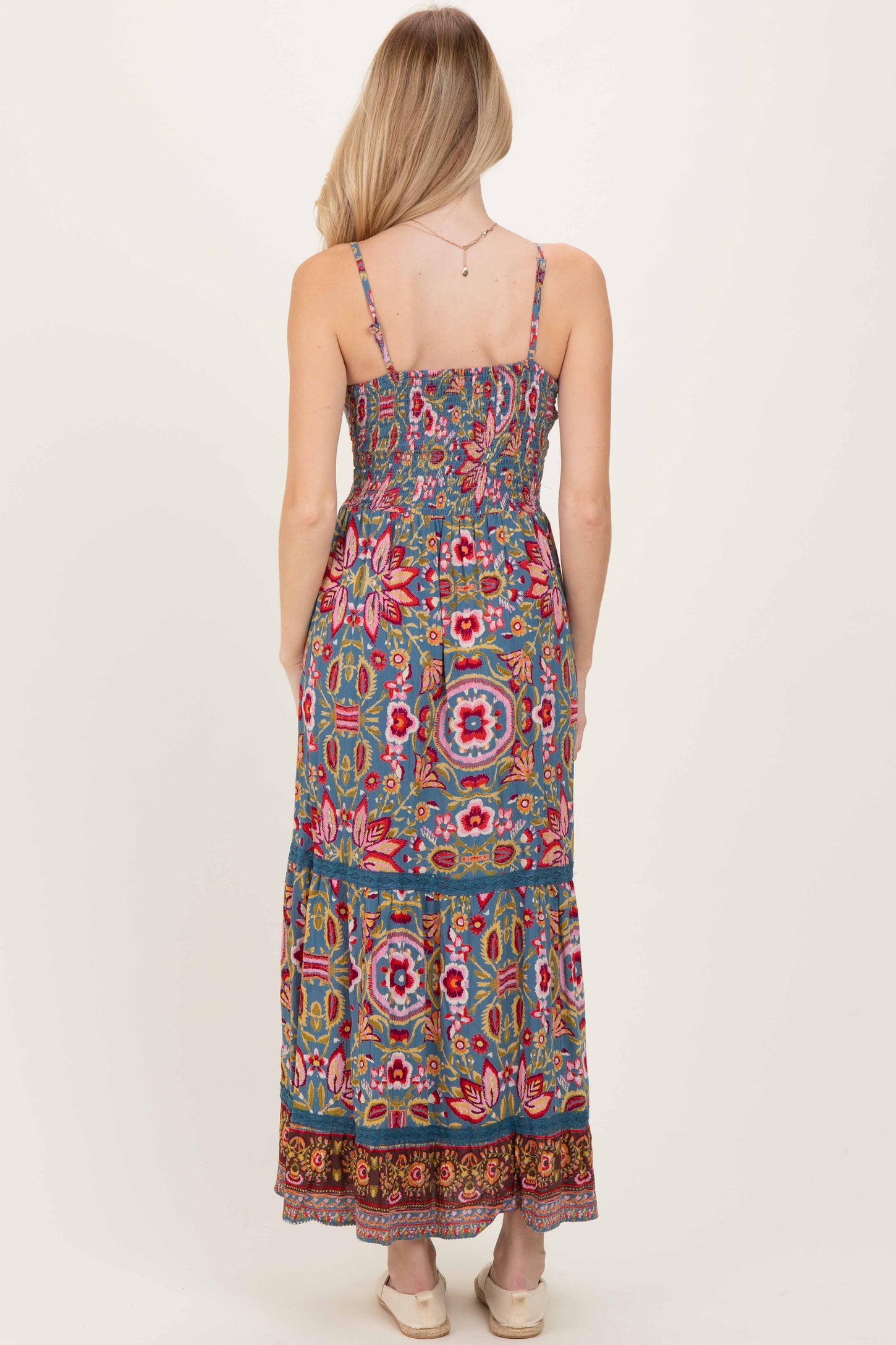 woman wearing a blue floral maxi dress with adjustable spaghetti straps and a smocked bodice, shown from the back