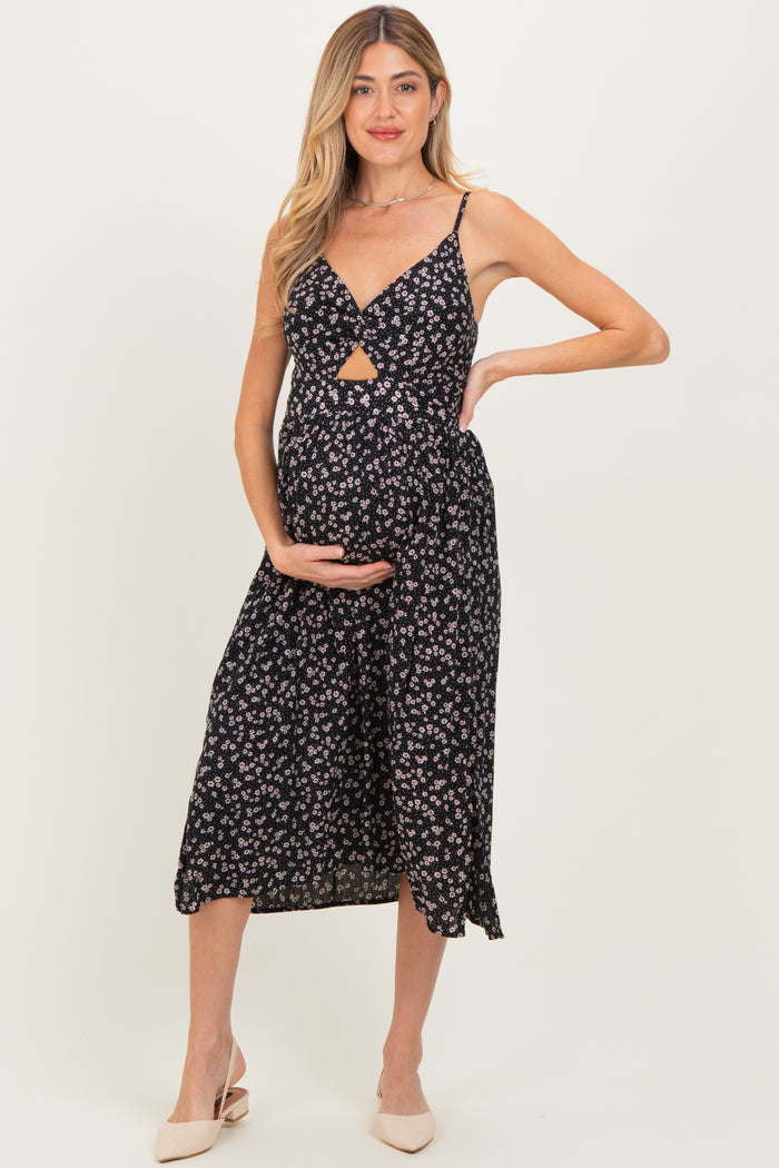 woman wearing a black floral maternity dress with a cutout under the bust and holding her baby bump