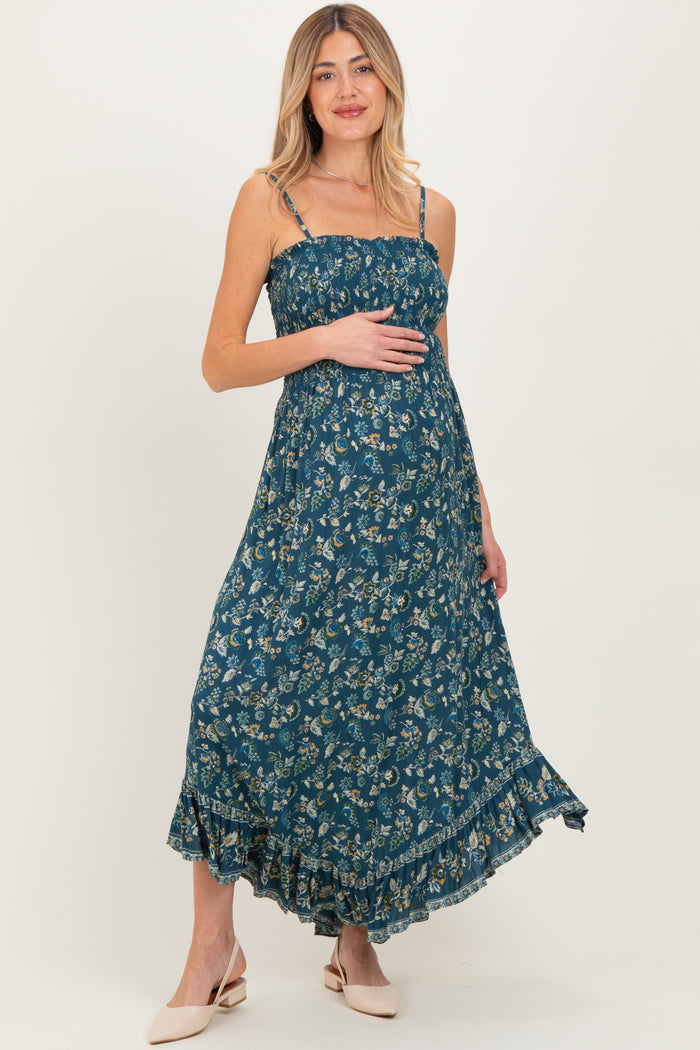 woman wearing a teal floral maternity maxi dress with adjustable straps and a ruffled hem, holding her baby bump