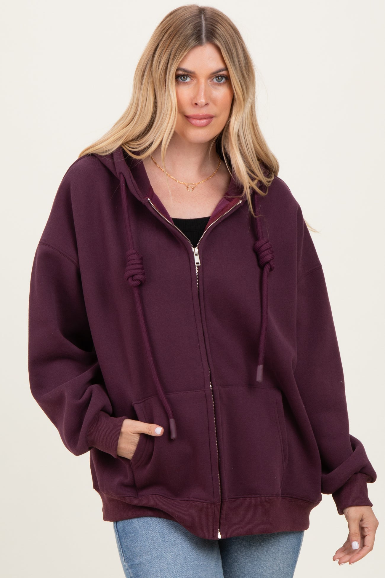 woman wearing a burgundy oversized zip-up hoodie with drawstrings and side pockets, styled with light blue jeans