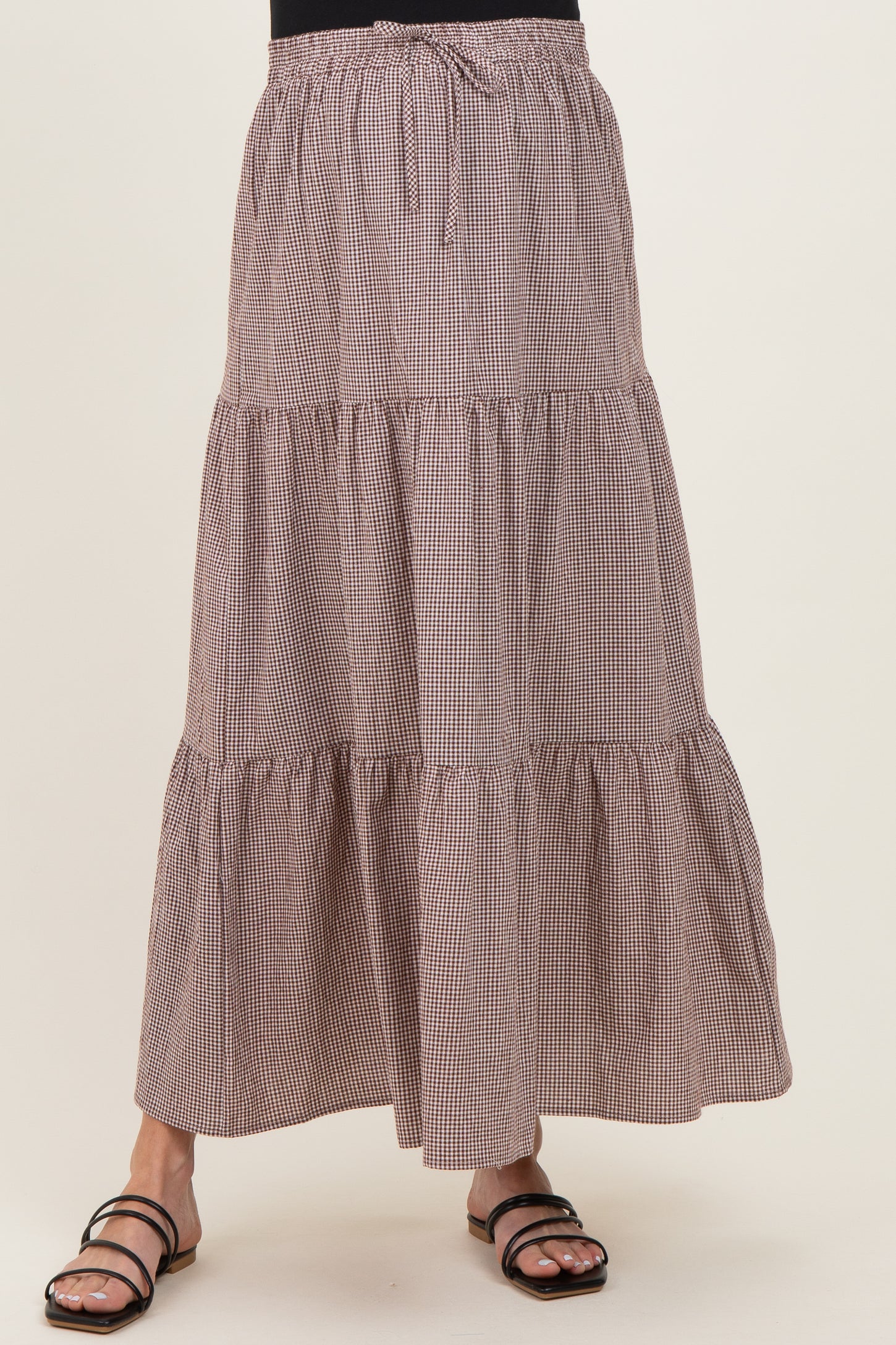 maternity wear in a brown and white checked maxi skirt with tiers and an adjustable tie waist, model wearing it