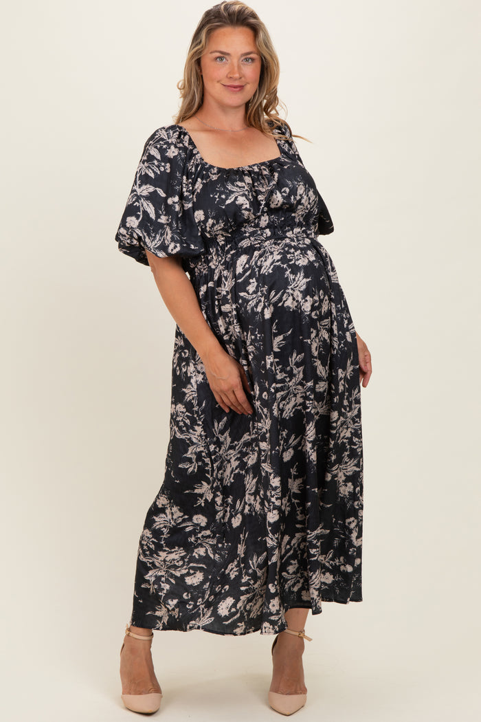 woman wearing a floral black maternity maxi dress with a square neckline and puff sleeves, holding her baby bump