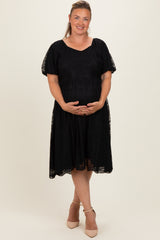 woman wearing a black maternity plus dress with short sleeves and lace detailing, holding her baby bump