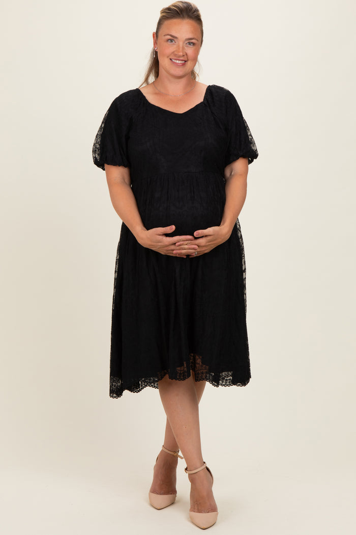 woman wearing a black maternity plus dress with short sleeves and lace detailing, holding her baby bump
