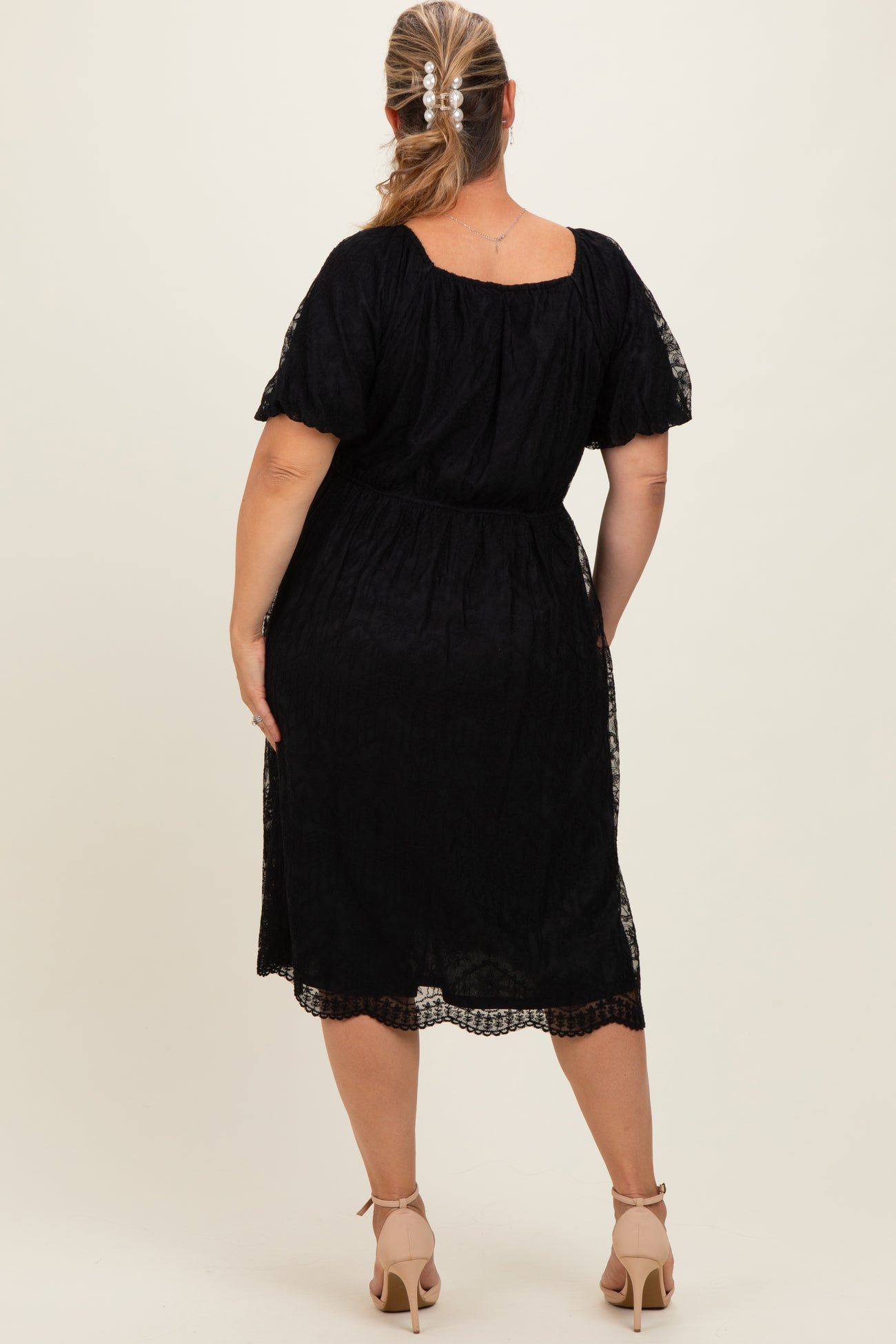 woman wearing a black maternity plus dress with a cinched waist and lace details, shown from the back