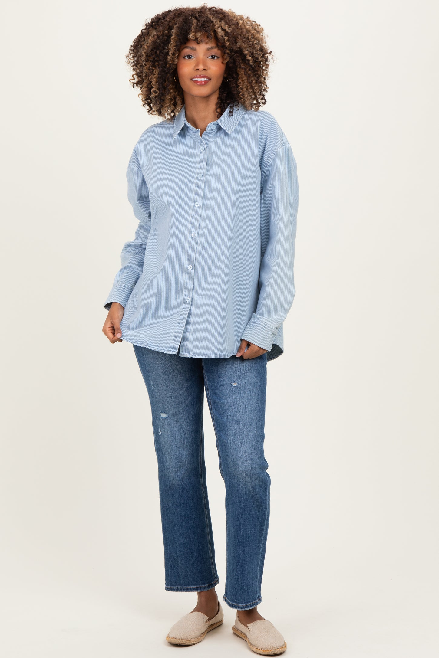 woman wearing a light blue striped maternity button-up shirt and distressed jeans, showing a baby bump