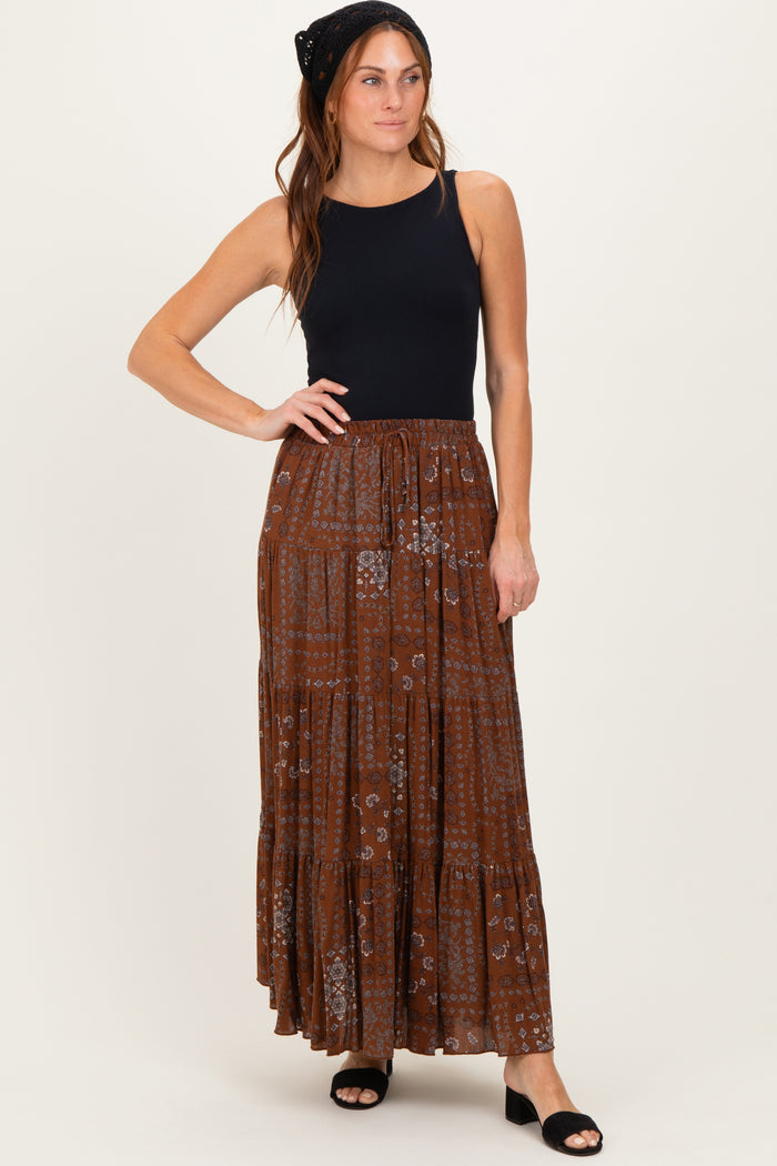 woman wearing a black sleeveless top and a brown floral maxi skirt, styled with a black headband and sandals