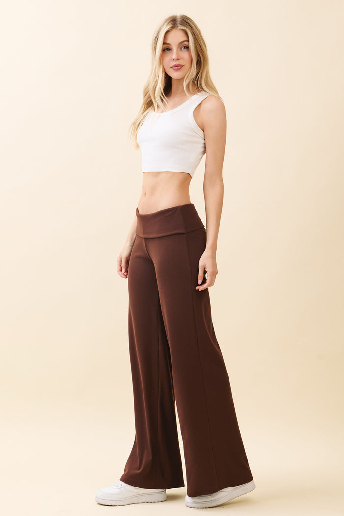 woman wearing a white crop top and brown wide leg pants, standing against a beige background