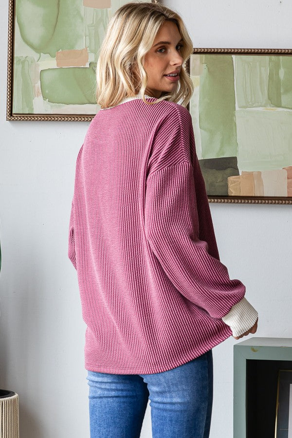 woman wearing a pink ribbed long-sleeve top with white cuffs and blue jeans, shown from the back