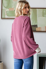 woman wearing a pink ribbed long-sleeve top with white cuffs and blue jeans, shown from the back