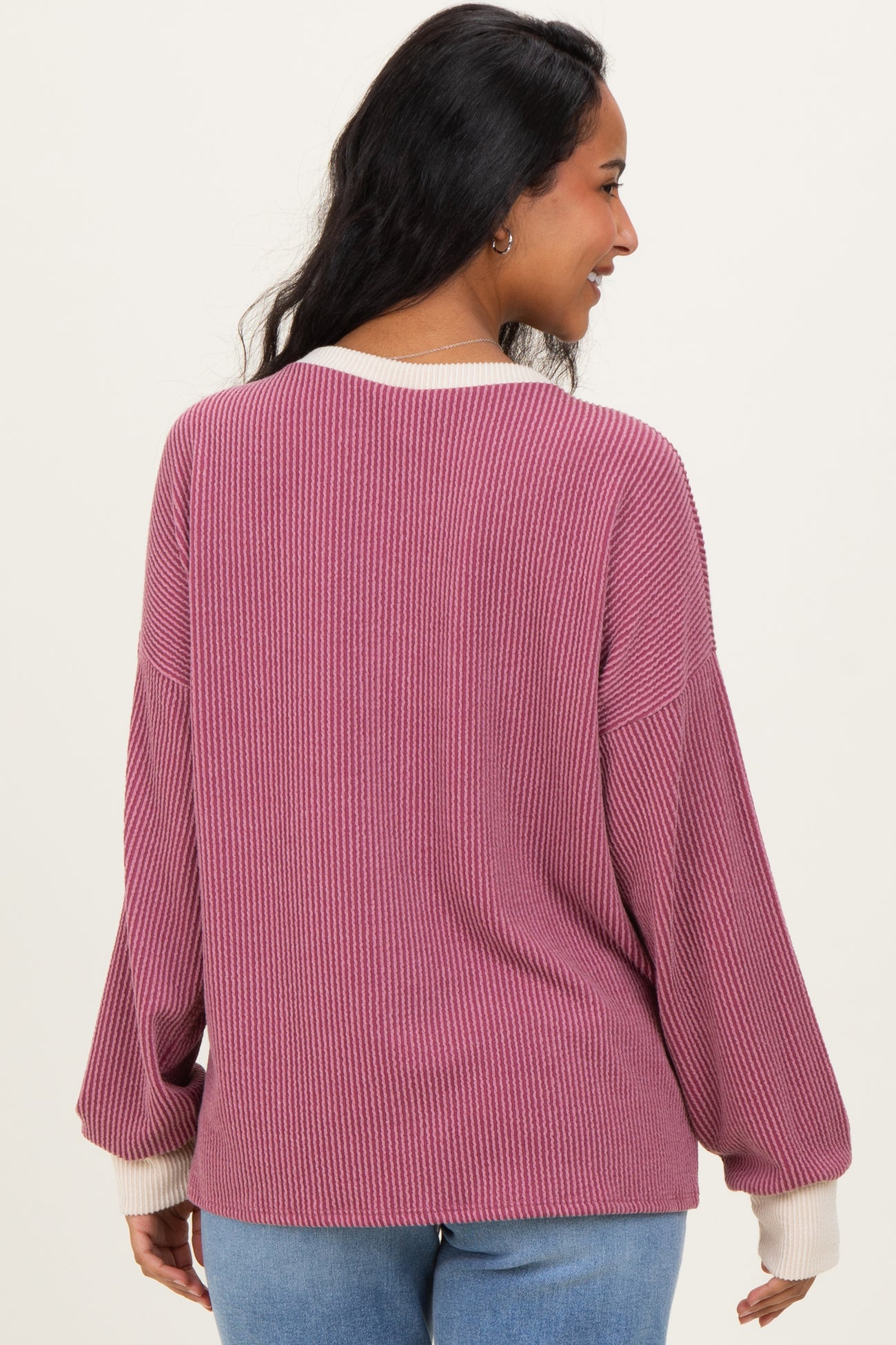 woman wearing a mauve oversized ribbed maternity sweater with white cuffs, showing her back and part of her pregnant belly