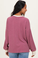 woman wearing a mauve oversized ribbed maternity sweater with white cuffs, showing her back and part of her pregnant belly