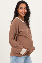 woman wearing a brown ribbed maternity sweater with light beige accents and a visible baby bump