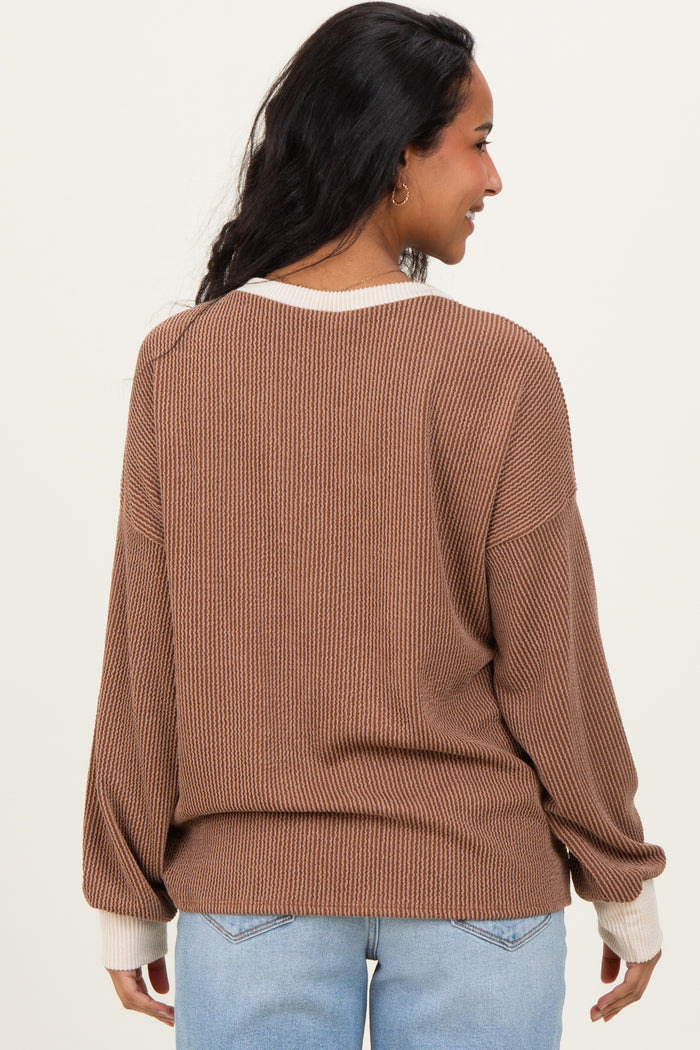 woman wearing a brown maternity sweater with contrast white cuffs, seen from the back with a relaxed fit