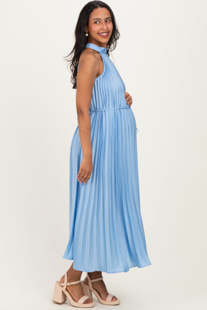 woman wearing a light blue pleated maternity dress with a halter neckline and holding her baby bump