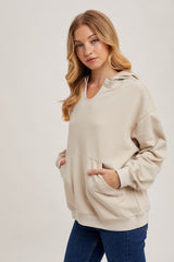 woman wearing a beige oversized hoodie with a front pocket and adjustable hood, paired with blue jeans