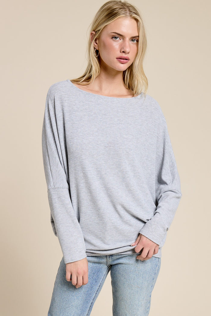 woman wearing a light gray oversized long sleeve top with a boat neckline and relaxed fit paired with blue jeans