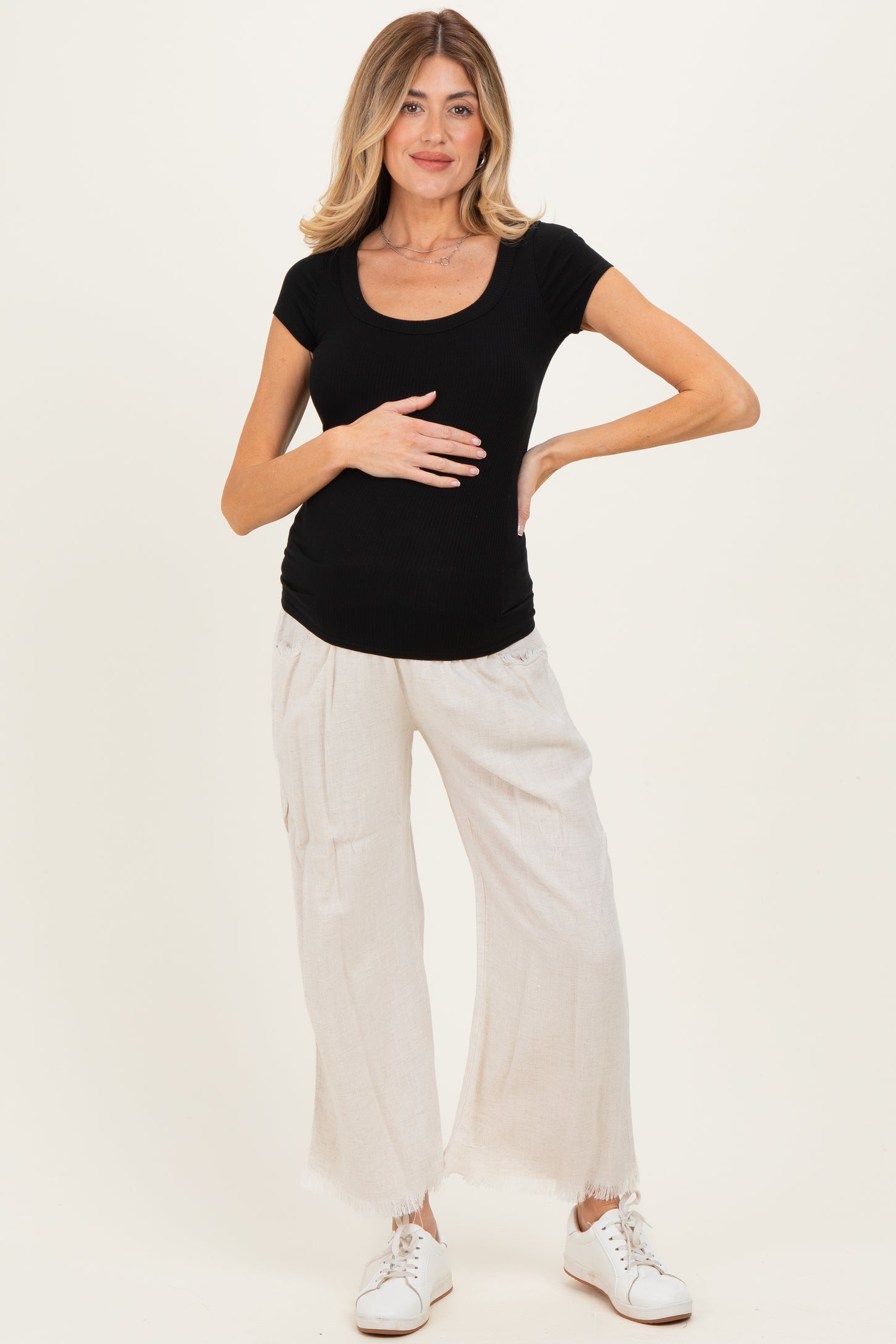 woman wearing a black short sleeve ribbed maternity top and light beige wide-leg pants, displaying her baby bump