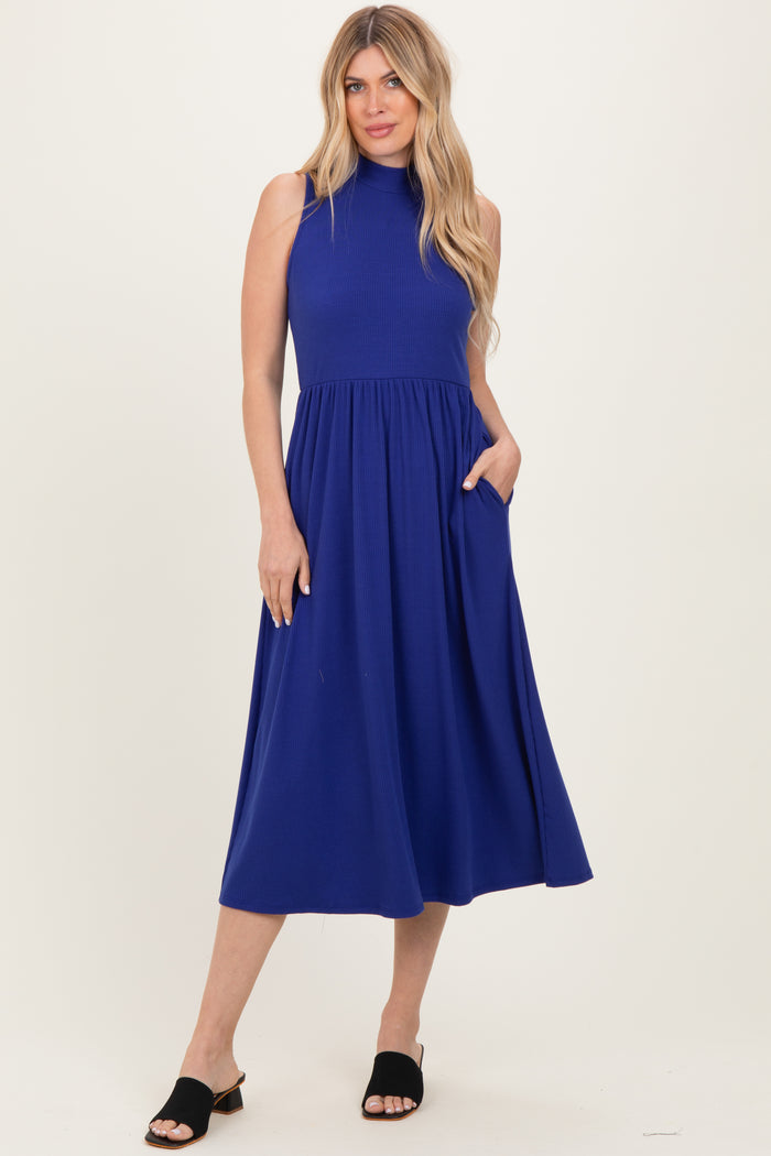 woman wearing a sleeveless royal blue midi dress with a high neck and pockets, standing in a relaxed pose
