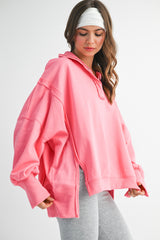 woman wearing an oversized pink pullover hoodie with a high neckline and side slits, paired with gray leggings