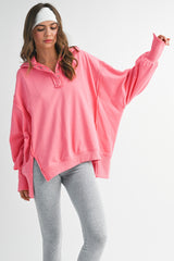 woman wearing a loose-fitting pink pullover with a collar and wide sleeves paired with gray leggings