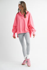 woman wearing a bright pink oversized pullover sweatshirt with a collared neckline, paired with gray leggings and pink sneakers