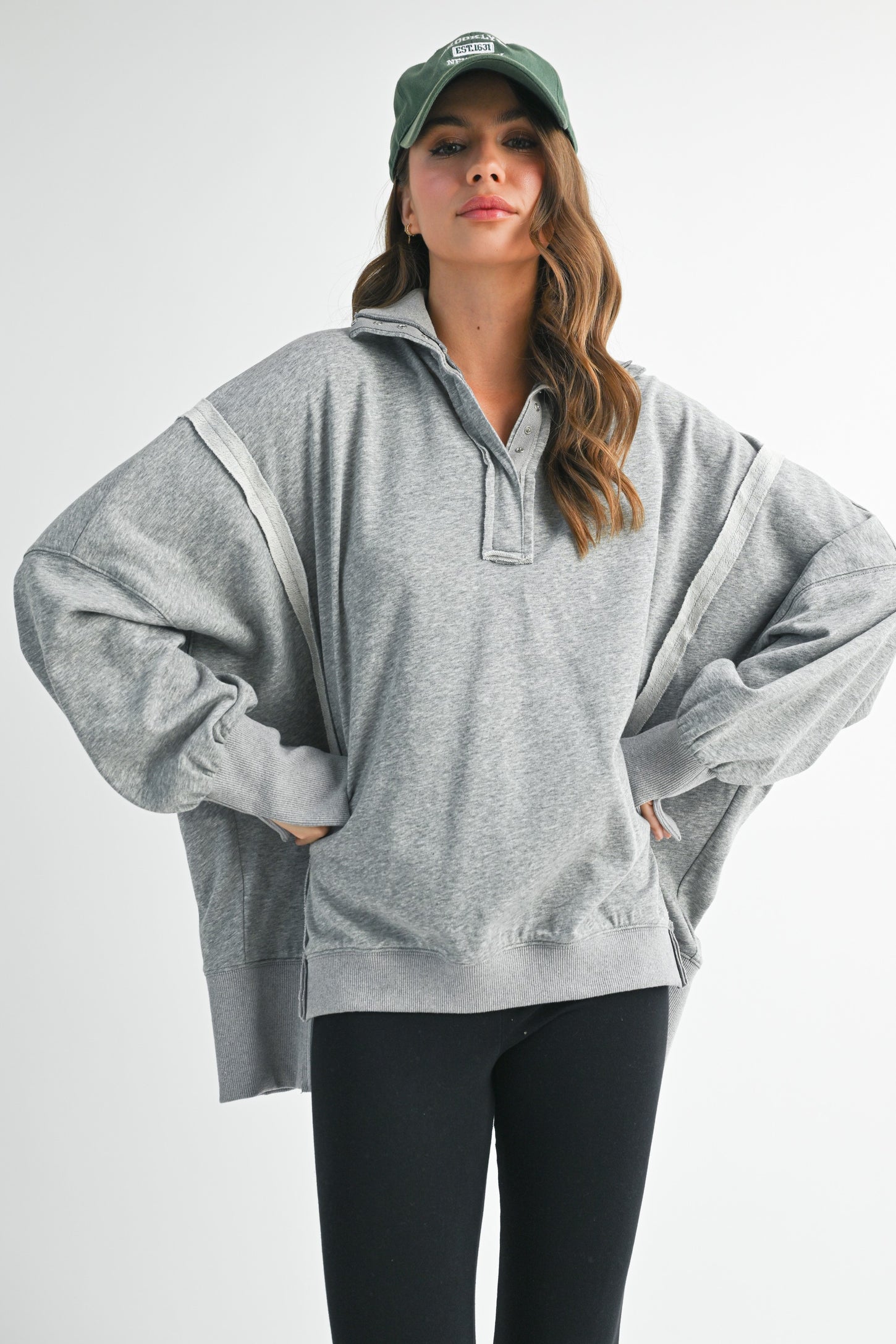 woman wearing an oversized gray pullover sweatshirt with a collared neck and ribbed cuffs, paired with black leggings