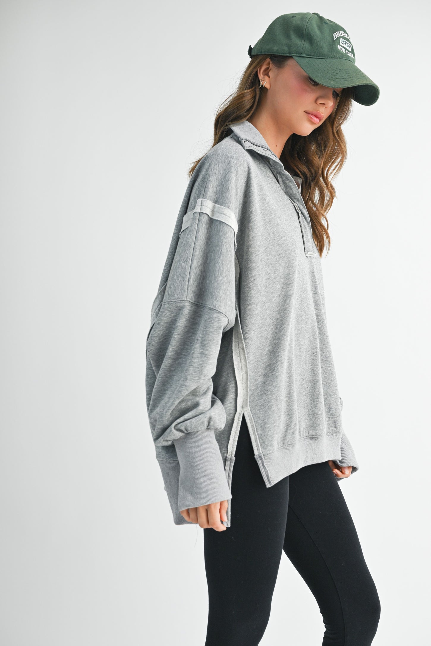 woman wearing a gray oversized pullover sweatshirt with side slits and black leggings, showing a casual look