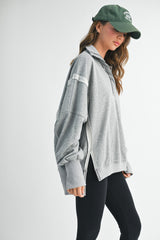 woman wearing a gray oversized pullover sweatshirt with side slits and black leggings, showing a casual look
