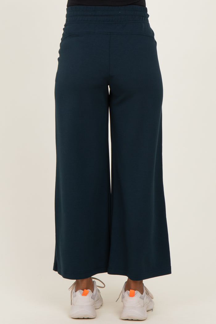 woman wearing dark teal maternity wide-leg pants, showing the back view with a comfortable waistband and casual sneakers