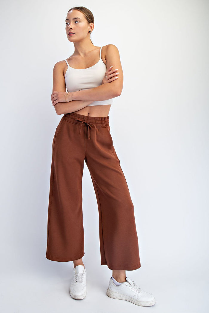 woman wearing a white cropped tank top and brown wide-leg pants with an elastic waistband, posing with arms crossed