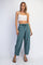 woman wearing a white cropped tank top and loose teal jogger pants, standing with hands on hips