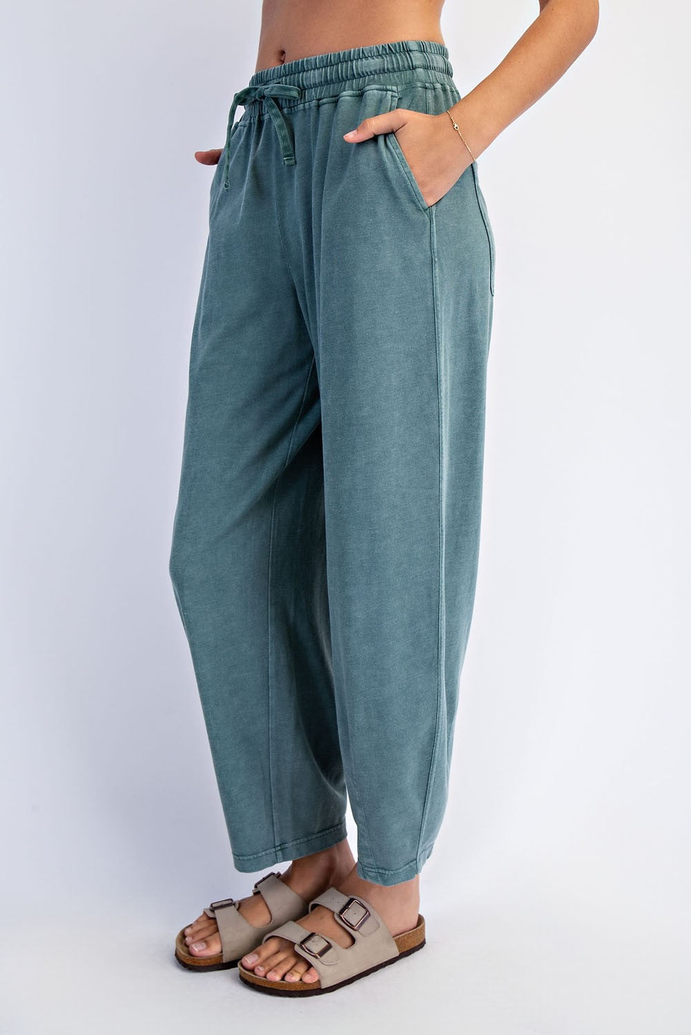 woman wearing teal loose-fitting sweatpants with an elastic waistband and pockets, paired with light sandals