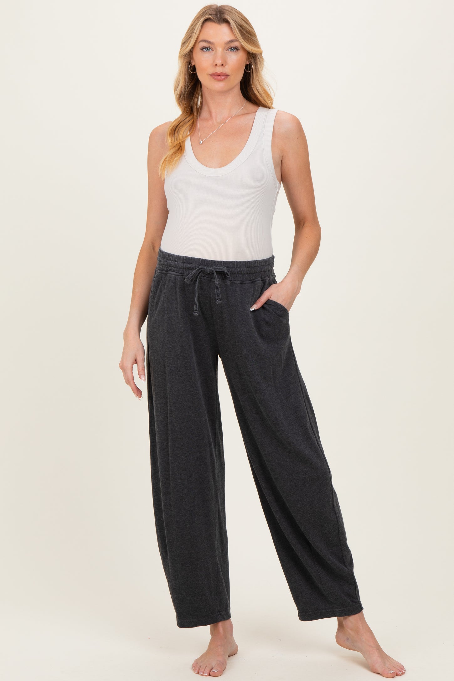 woman wearing a white ribbed tank top and dark gray maternity lounge pants with pockets and a drawstring waistband