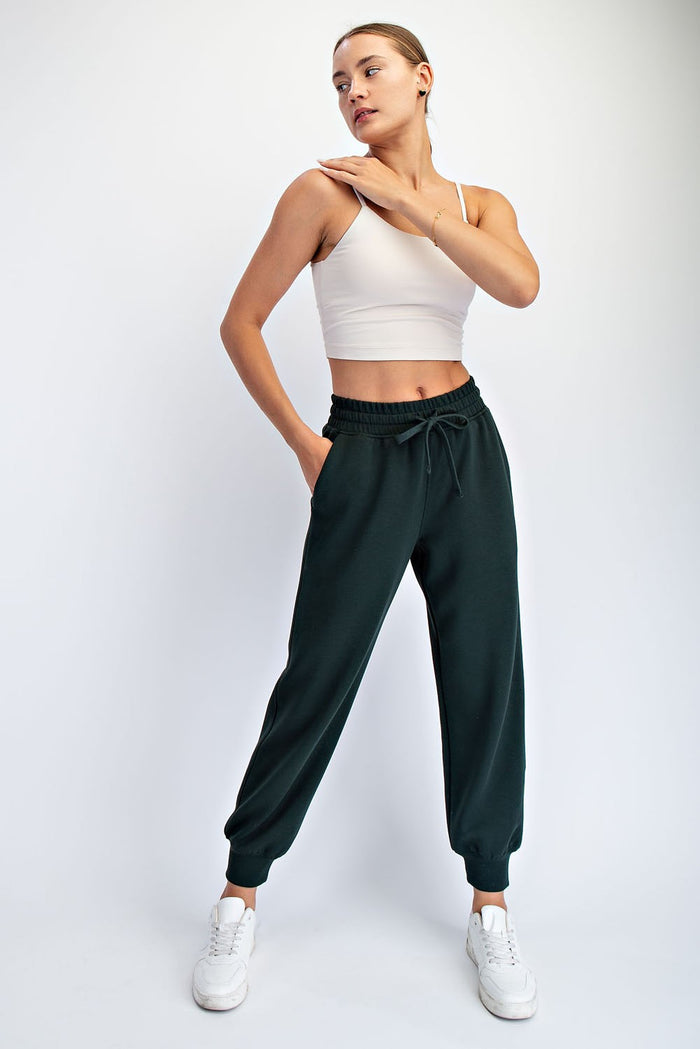 woman wearing a cream cropped tank top and dark green jogger pants with elastic waistband and cuffs