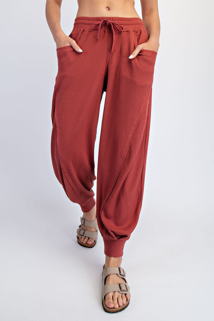 woman wearing rust-colored ribbed harem pants with pockets and drawstring waist, paired with casual sandals