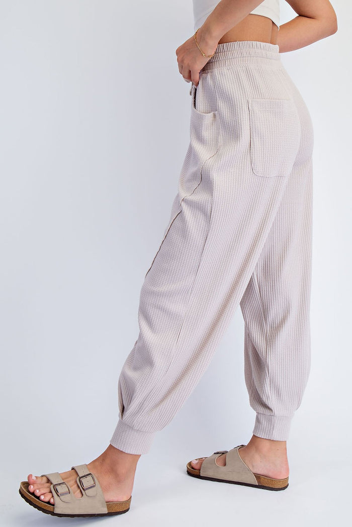 woman wearing light beige ribbed jogger pants with side pockets and adjustable waistband, styled with sandals