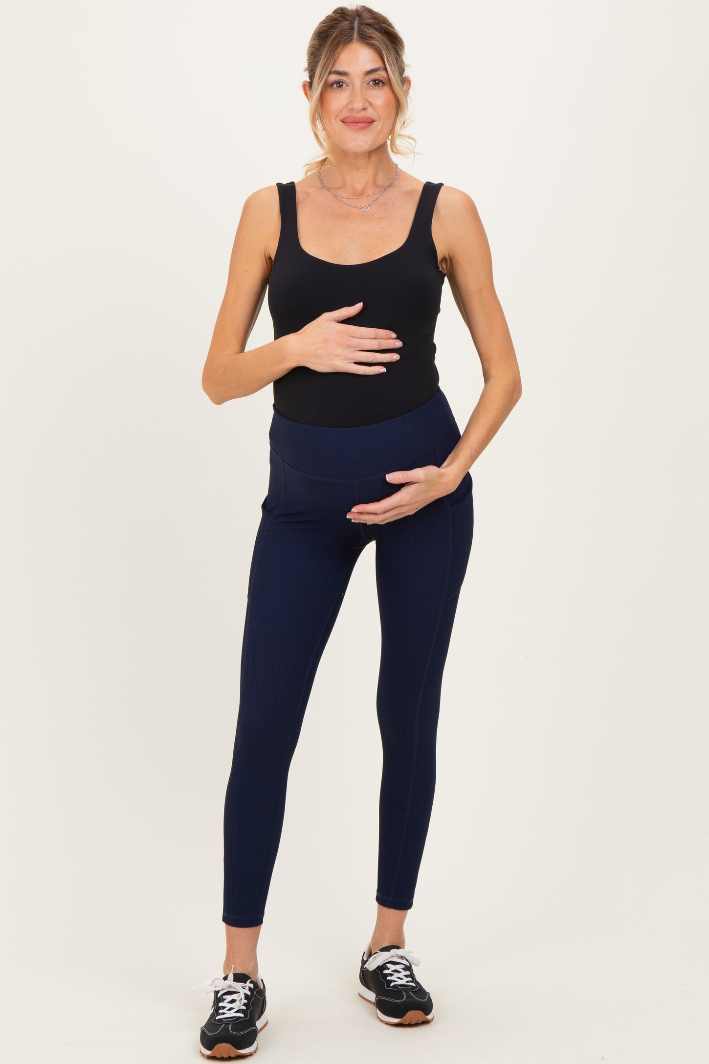 woman wearing a black maternity tank top and navy maternity leggings with a visible baby bump