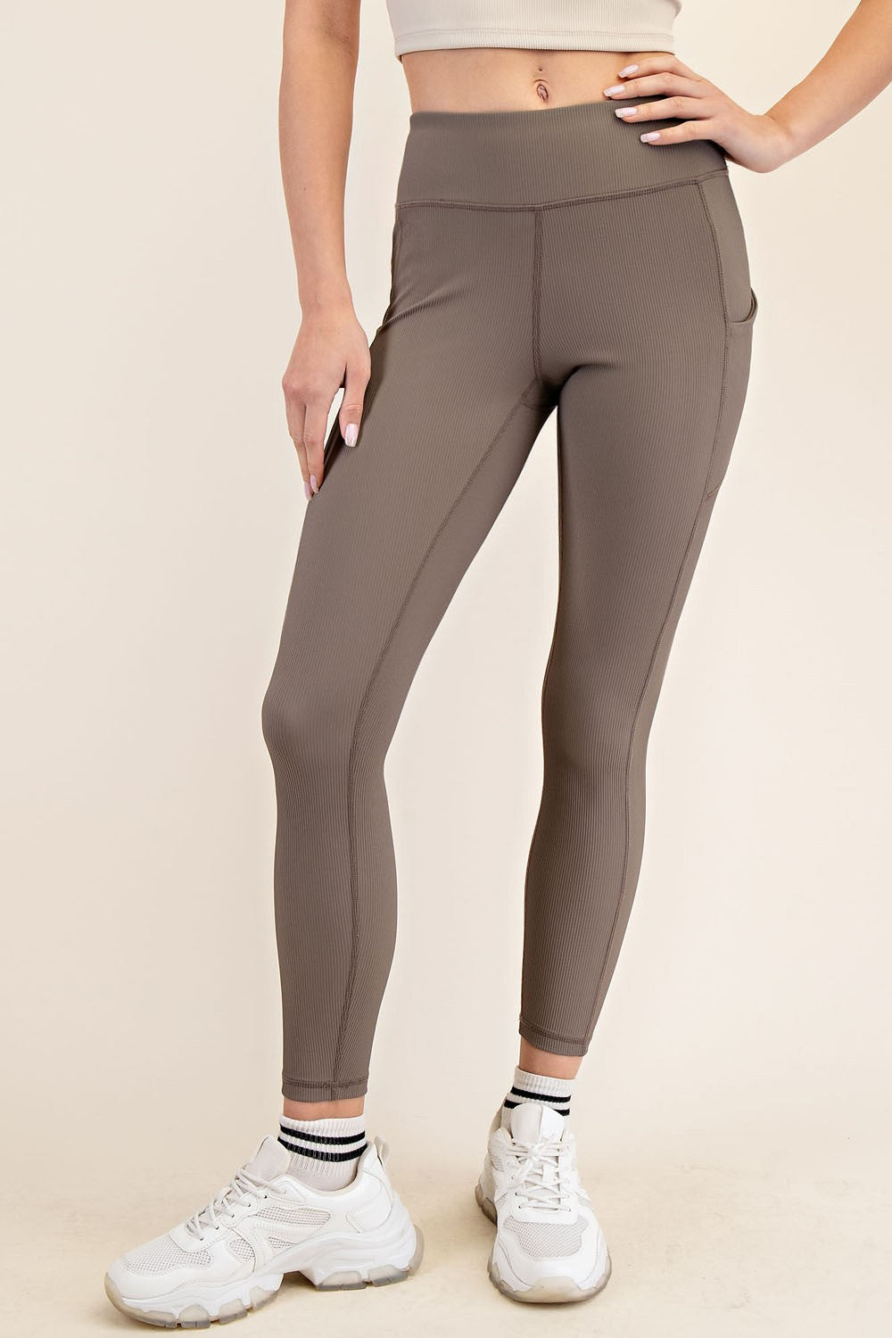 woman wearing brown high-waisted leggings with side pockets and white sneakers