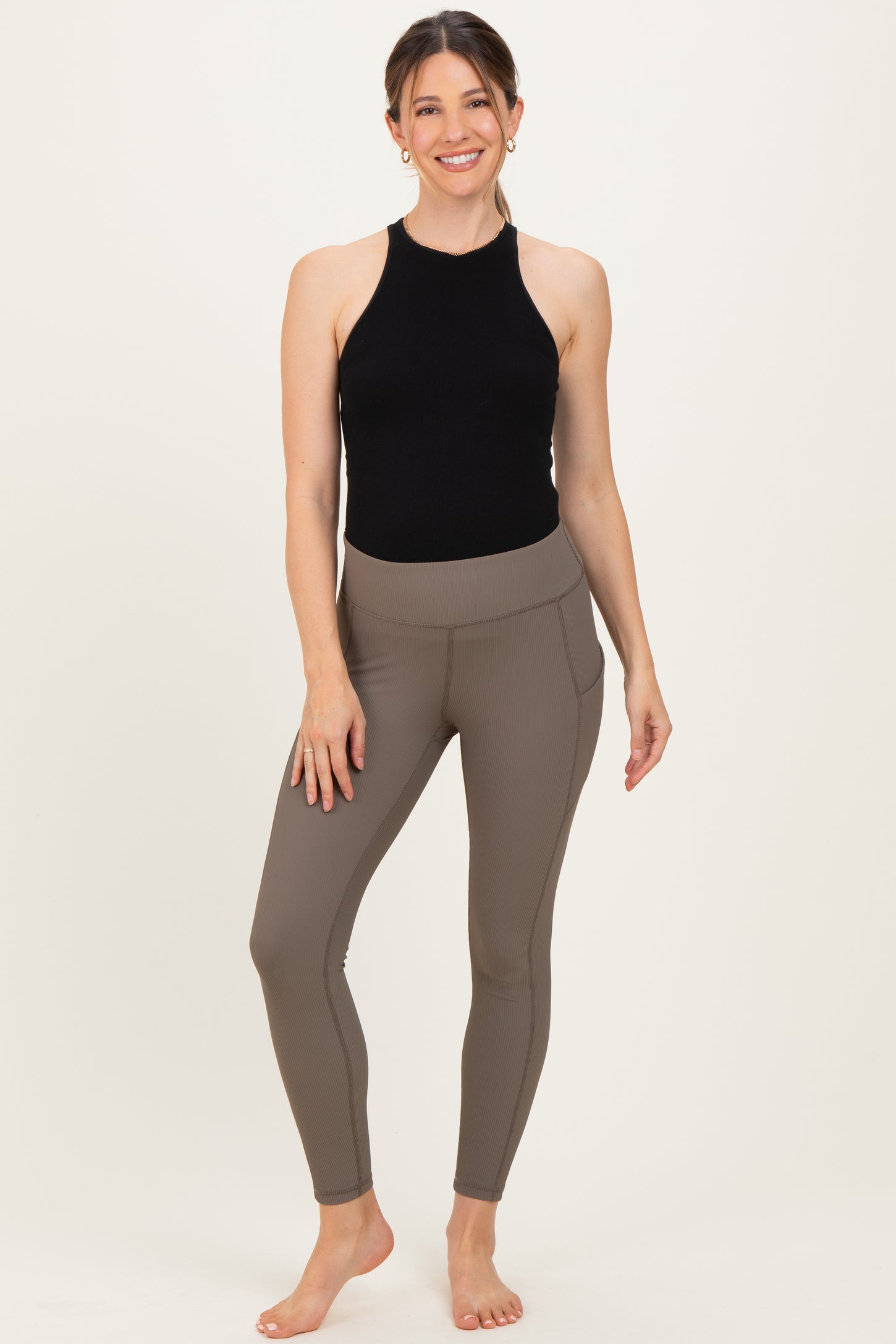 woman wearing a black halter neck maternity top and brown ribbed maternity leggings with side pockets