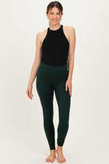 woman wearing a black halter top and dark green maternity leggings, showing a baby bump