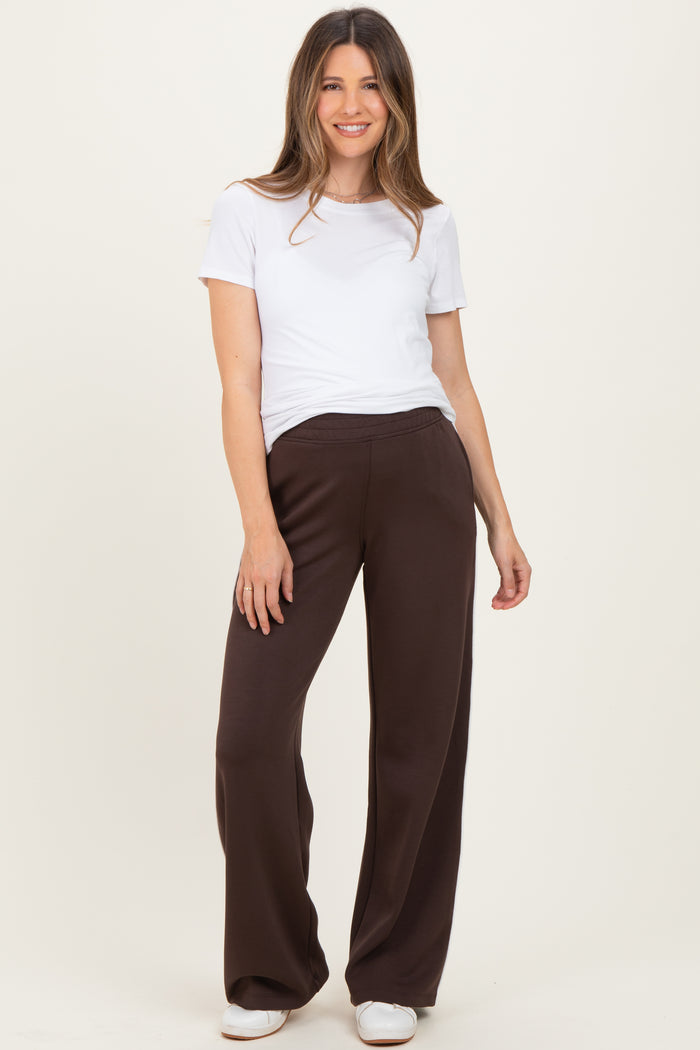 woman wearing a white short sleeve top and brown maternity wide-leg pants, posing with a relaxed smile