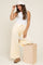 woman wearing a ribbed white tank top and yellow maternity lounge pants, posing with a bucket hat on a wooden block