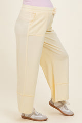 woman wearing light yellow maternity wide-leg sweatpants with pockets and a drawstring waistband, showing her baby bump