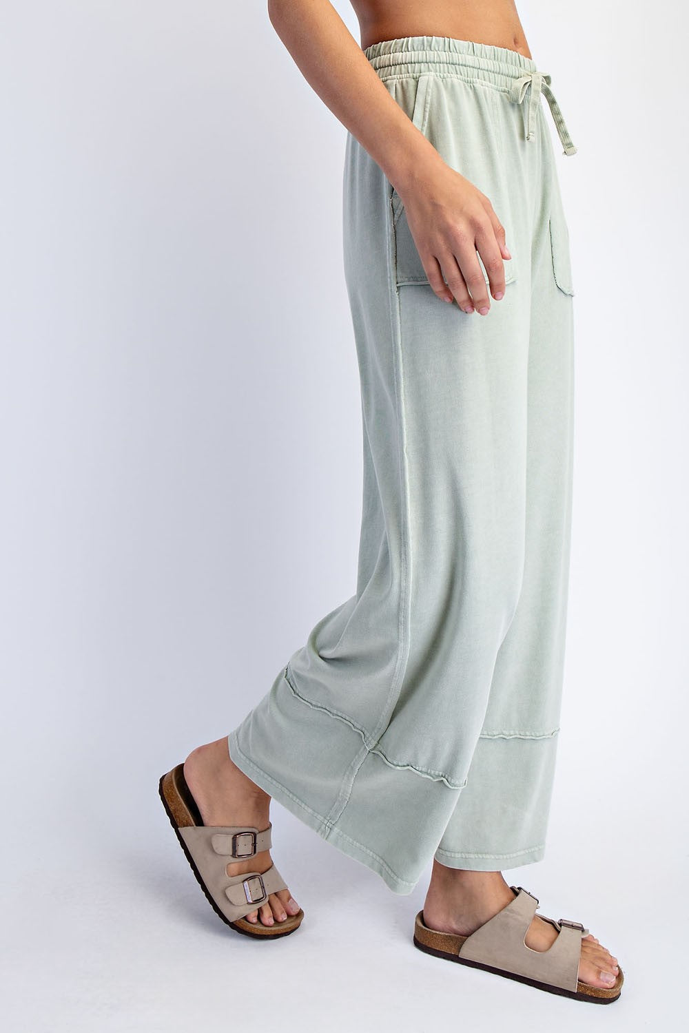 woman wearing light green wide-leg pants with side pockets and adjustable drawstring, paired with beige slide sandals