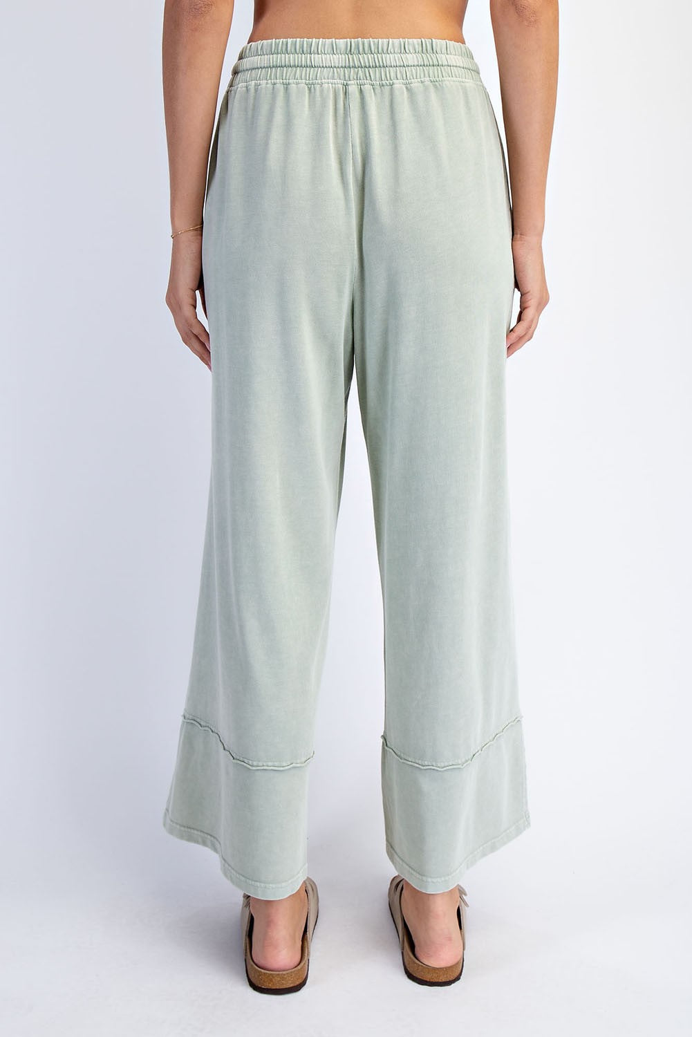 woman wearing light green wide-leg pants with a flowy hem and an elastic waistband, viewed from the back